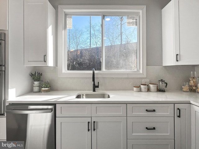 kitchen with decorative backsplash, white cabinets, dishwasher, light countertops, and a sink