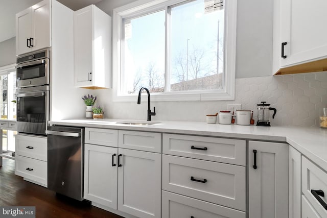 kitchen featuring stainless steel appliances, light countertops, decorative backsplash, white cabinetry, and a sink