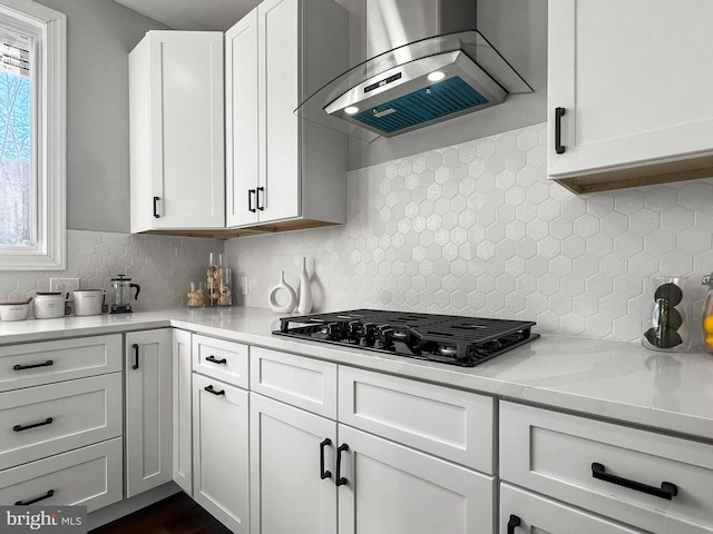 kitchen with light countertops, wall chimney range hood, black gas stovetop, and white cabinetry