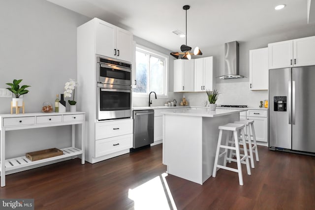 kitchen featuring a breakfast bar, appliances with stainless steel finishes, dark wood-type flooring, white cabinets, and wall chimney range hood