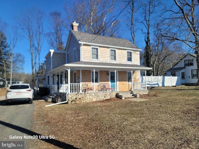 farmhouse-style home featuring covered porch, a chimney, roof with shingles, and fence