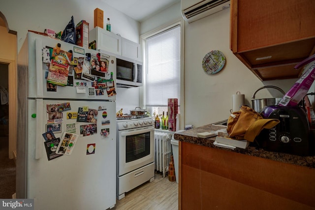 kitchen with white appliances, white cabinets, light wood-style floors, an AC wall unit, and radiator heating unit