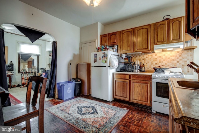 kitchen with arched walkways, white appliances, brown cabinetry, and under cabinet range hood