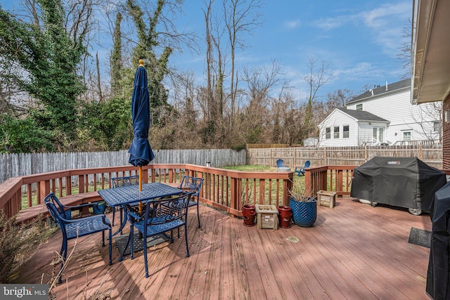 wooden deck featuring outdoor dining space, area for grilling, and a fenced backyard