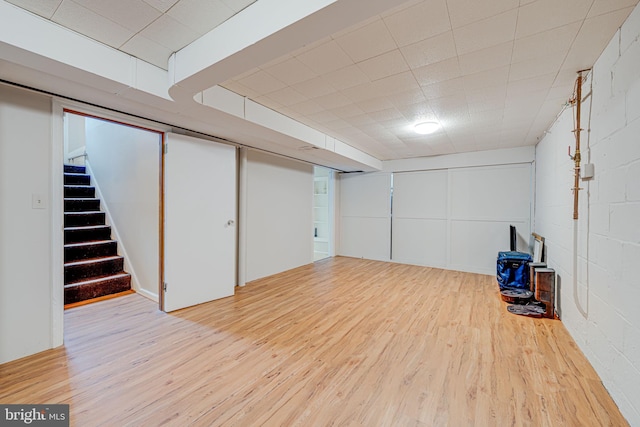 finished below grade area featuring stairway, wood finished floors, and concrete block wall