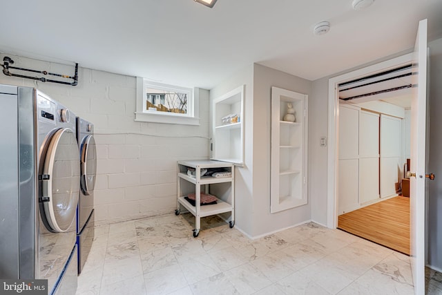 clothes washing area with concrete block wall, laundry area, built in features, washer and clothes dryer, and marble finish floor