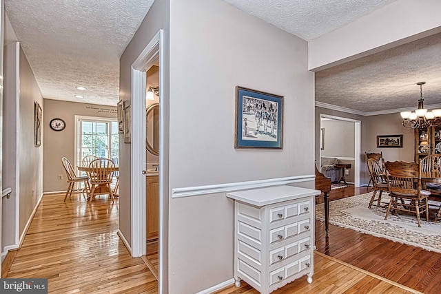 hallway with light wood-type flooring, baseboards, a chandelier, and a textured ceiling