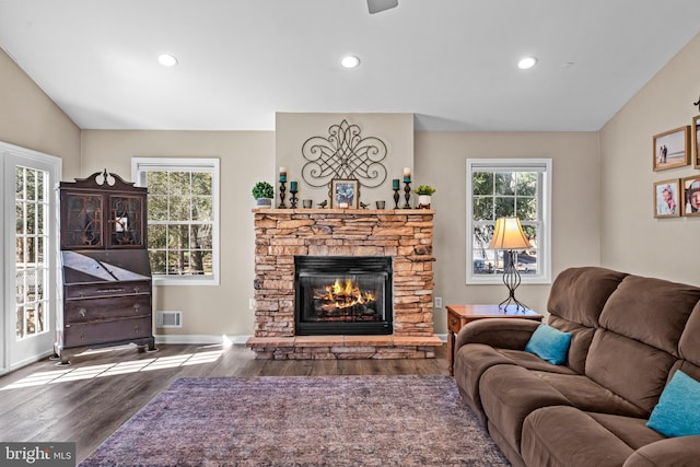 living area with visible vents, vaulted ceiling, a stone fireplace, wood finished floors, and baseboards