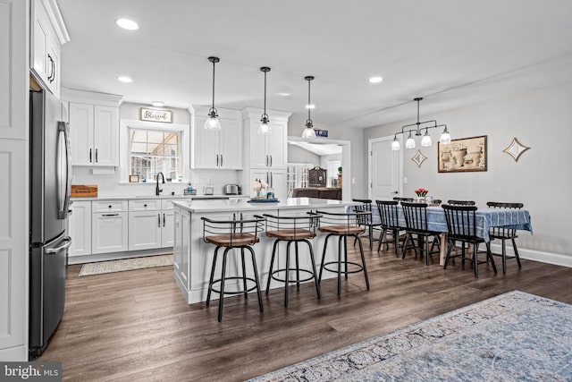 kitchen with white cabinets, a kitchen breakfast bar, freestanding refrigerator, light countertops, and a sink