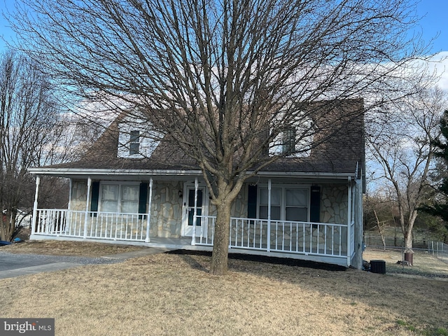 view of front of property featuring stone siding, a porch, a front lawn, and fence