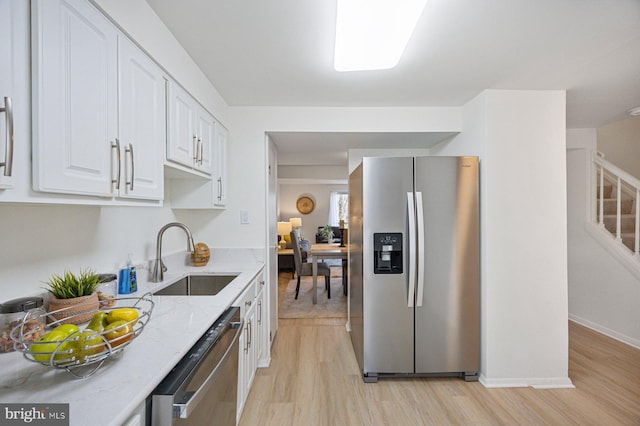 kitchen featuring light stone counters, stainless steel appliances, a sink, white cabinetry, and light wood finished floors