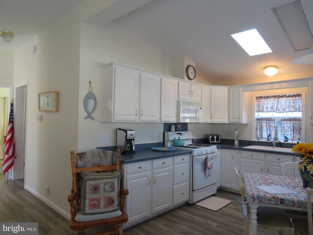 kitchen with white appliances, wood finished floors, a sink, white cabinets, and lofted ceiling with skylight