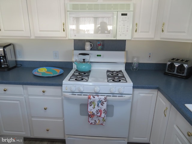 kitchen featuring white appliances, dark countertops, and white cabinets