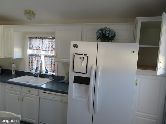 kitchen with dark countertops, white appliances, white cabinets, and a sink