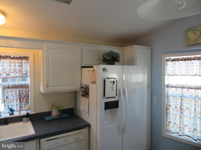 kitchen featuring white appliances, dark countertops, vaulted ceiling, white cabinetry, and a sink