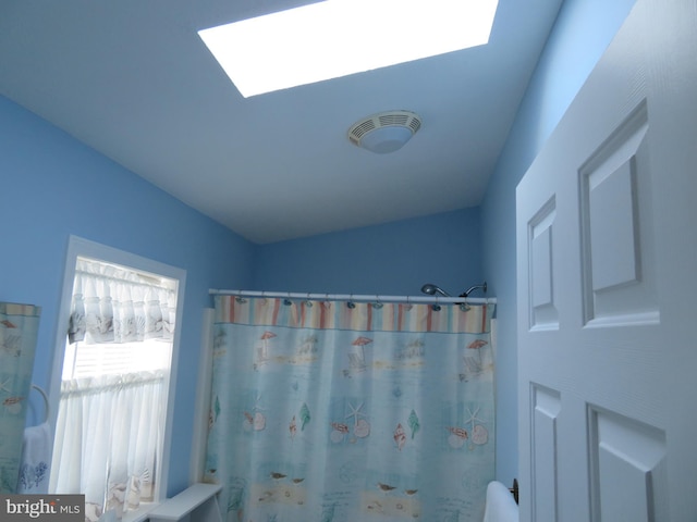 full bathroom with vaulted ceiling with skylight, a shower with shower curtain, and visible vents