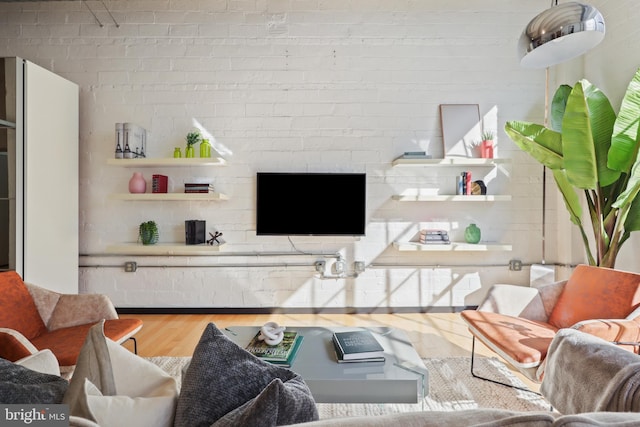 living area with brick wall and wood finished floors