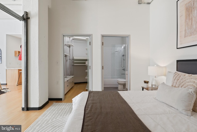 bedroom featuring ensuite bathroom, light wood finished floors, and a walk in closet