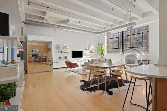 dining area with brick wall, light wood-style flooring, a high ceiling, and beam ceiling