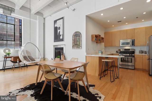 dining room with light wood-style flooring, a towering ceiling, a high end fireplace, and recessed lighting