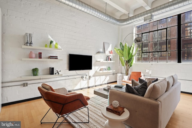 living room featuring brick wall, light wood-style flooring, and beamed ceiling