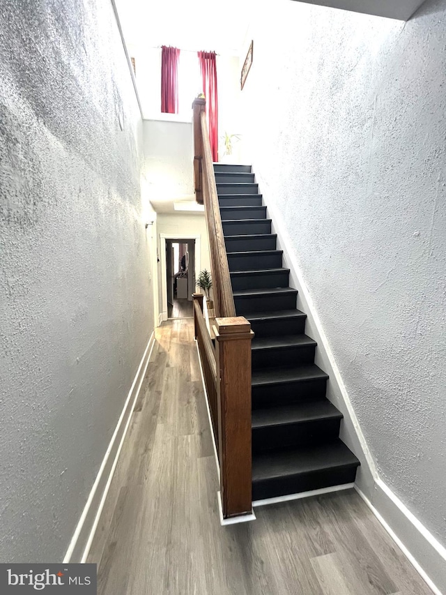 stairway with a textured wall, wood finished floors, and baseboards