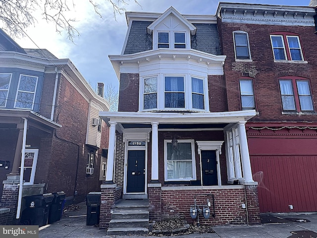 view of front of house with brick siding, mansard roof, and a porch