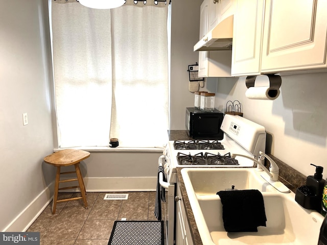 kitchen featuring visible vents, tile patterned flooring, under cabinet range hood, baseboards, and white gas range oven