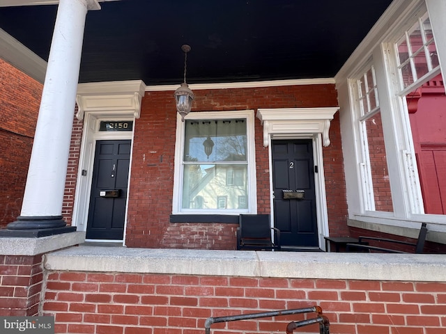 doorway to property featuring covered porch and brick siding