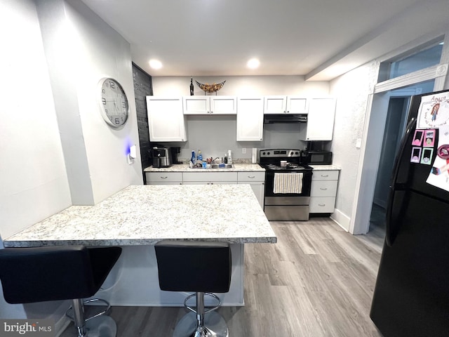 kitchen featuring light wood-style flooring, under cabinet range hood, black appliances, and a kitchen bar