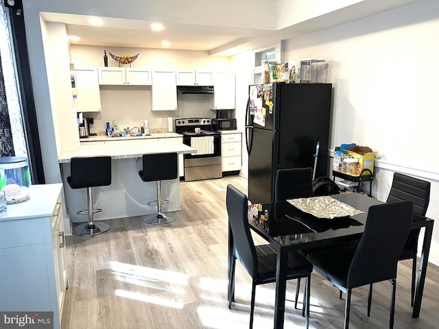 kitchen with light countertops, a peninsula, light wood-type flooring, under cabinet range hood, and black appliances