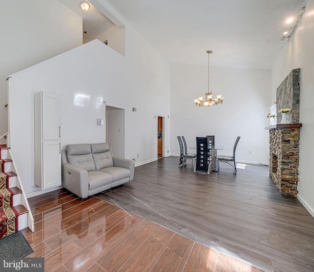 living area with baseboards, stairway, wood finished floors, high vaulted ceiling, and a notable chandelier