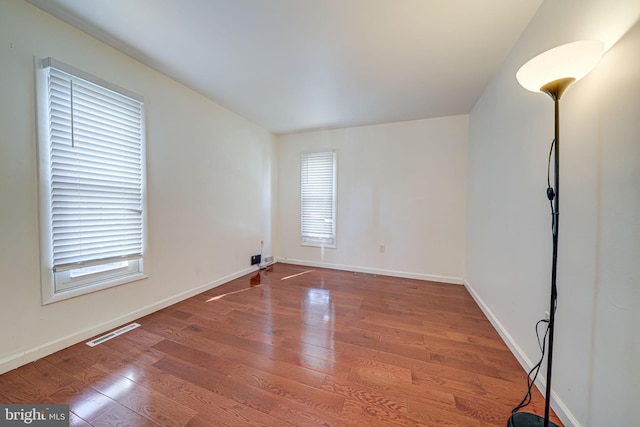 empty room featuring wood finished floors, visible vents, and a healthy amount of sunlight