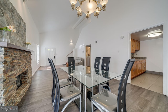 dining room featuring high vaulted ceiling, a fireplace, a chandelier, and wood finished floors