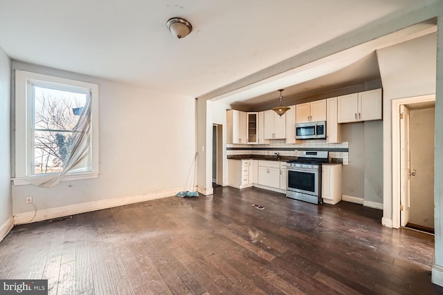 kitchen with dark wood finished floors, stainless steel appliances, dark countertops, tasteful backsplash, and baseboards