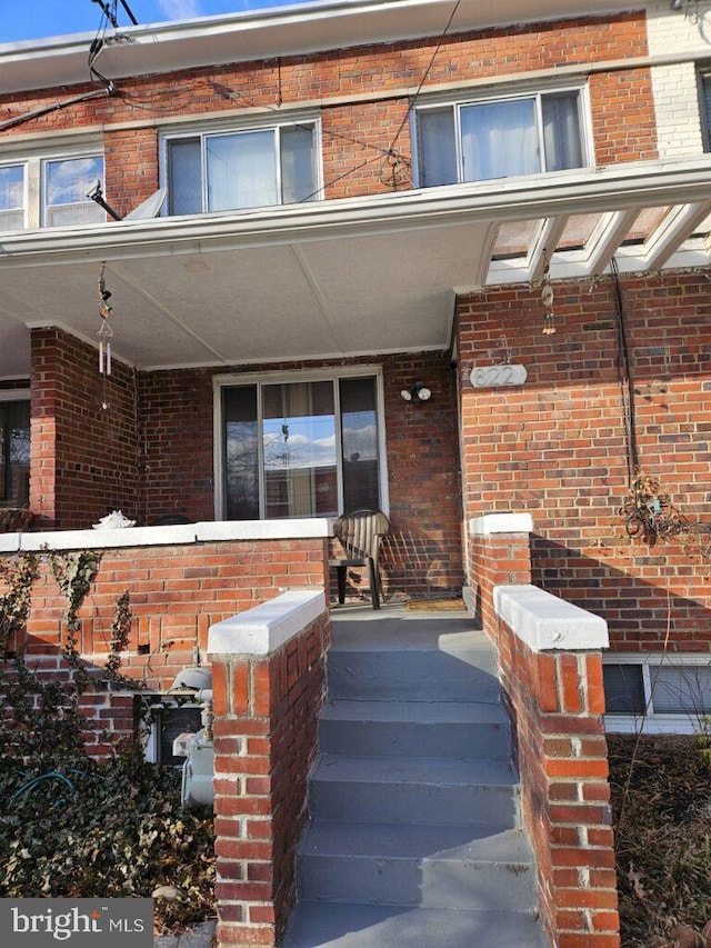 view of exterior entry with a porch and brick siding