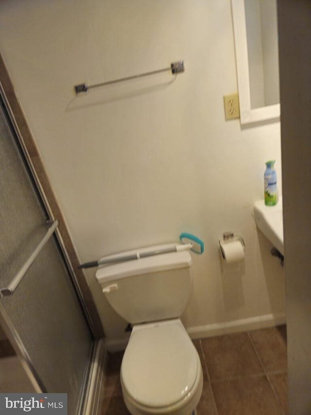 bathroom with toilet, a shower with door, tile patterned flooring, and baseboards