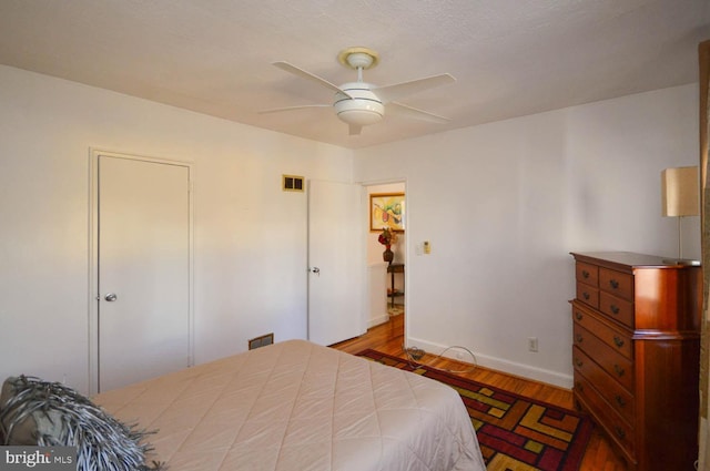 bedroom with a ceiling fan, baseboards, visible vents, and wood finished floors