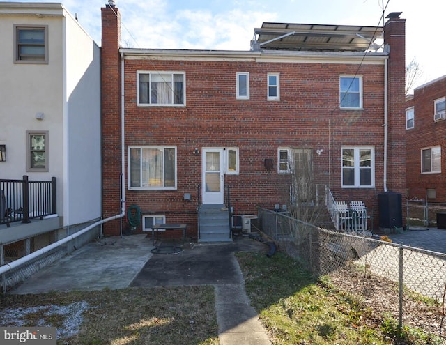 rear view of house with entry steps, central AC unit, brick siding, fence, and a chimney