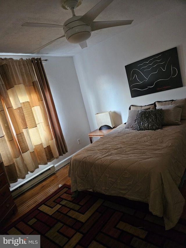 bedroom featuring ceiling fan, a baseboard heating unit, and wood finished floors