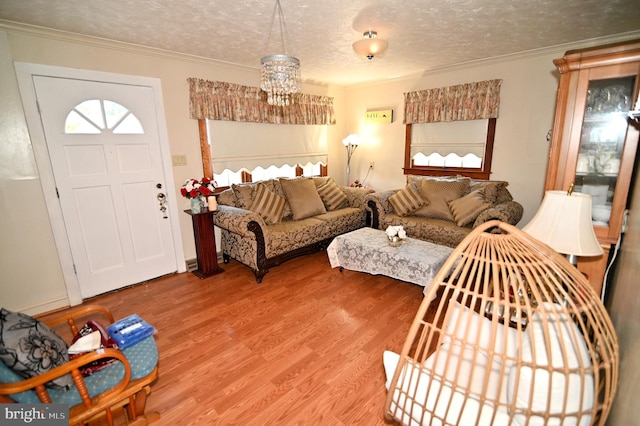 living room featuring a textured ceiling, ornamental molding, wood finished floors, and an inviting chandelier