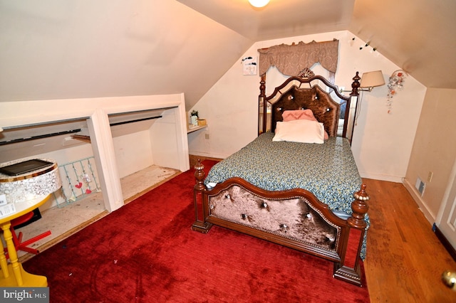 bedroom with vaulted ceiling, wood finished floors, and baseboards