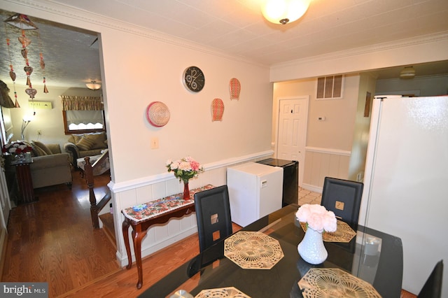 dining space featuring crown molding, visible vents, wood finished floors, and wainscoting