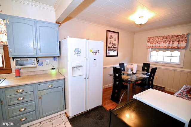 kitchen featuring wainscoting, light countertops, crown molding, blue cabinetry, and white fridge with ice dispenser