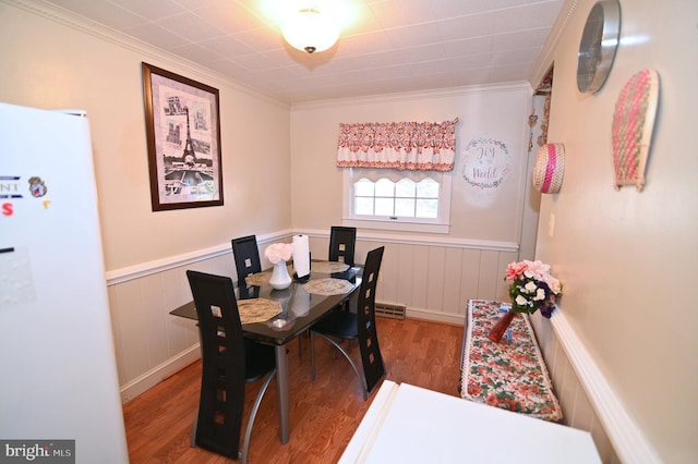 dining area featuring a wainscoted wall, crown molding, and wood finished floors