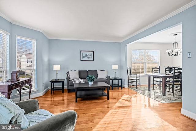 living area featuring a chandelier, crown molding, light wood-style floors, and baseboards