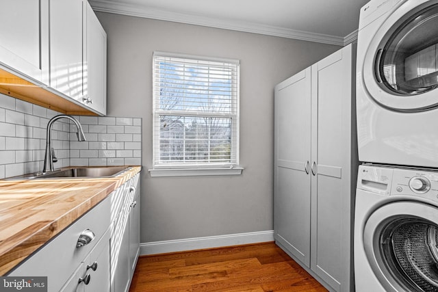 laundry area with cabinet space, wood finished floors, crown molding, stacked washing maching and dryer, and a sink