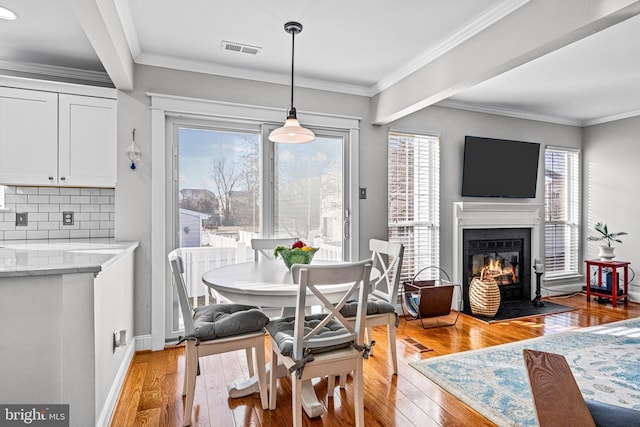 dining area with light wood-type flooring, a glass covered fireplace, visible vents, and a healthy amount of sunlight