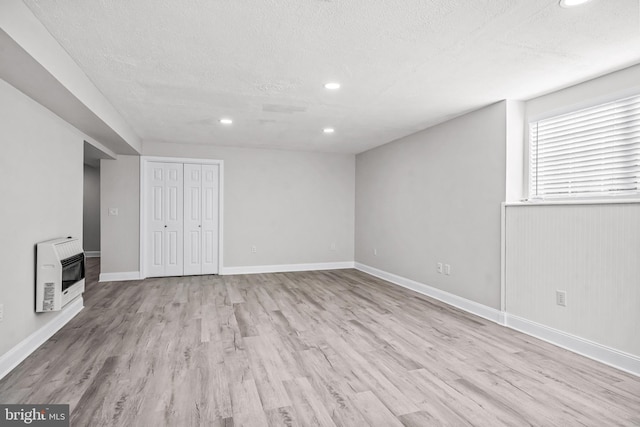 basement with baseboards, a textured ceiling, heating unit, and wood finished floors