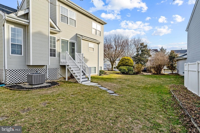 rear view of property featuring a lawn, fence, and central air condition unit